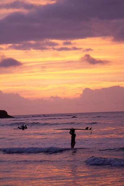 Woman holding surfboard overhead in water at sunset