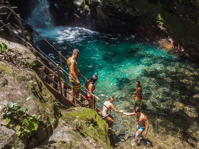 A group of people standing on top of a cliff next to a waterfall.