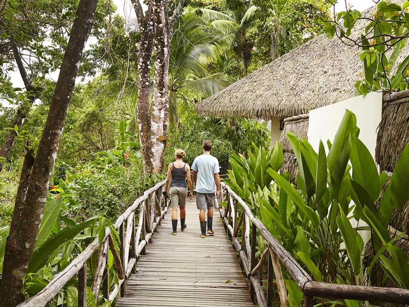 A couple of people walking across a wooden bridge.