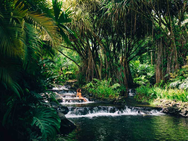 A woman is sitting on a small waterfall in the jungle.