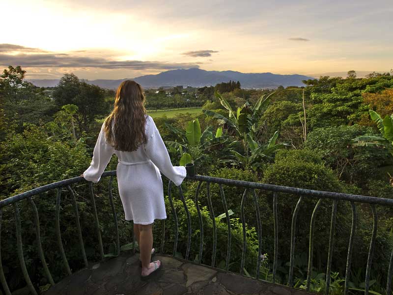 A woman standing on a balcony overlooking a lush green valley.